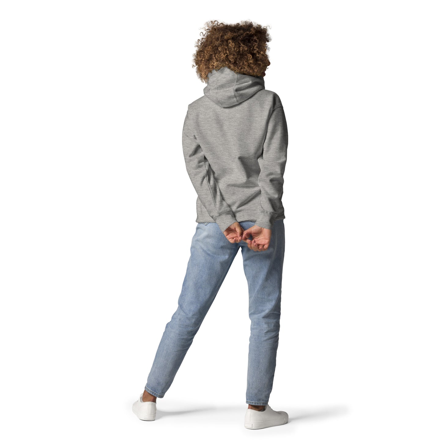 Person with curly hair wearing a grey unisex hoodie and light blue jeans, standing with hands behind back