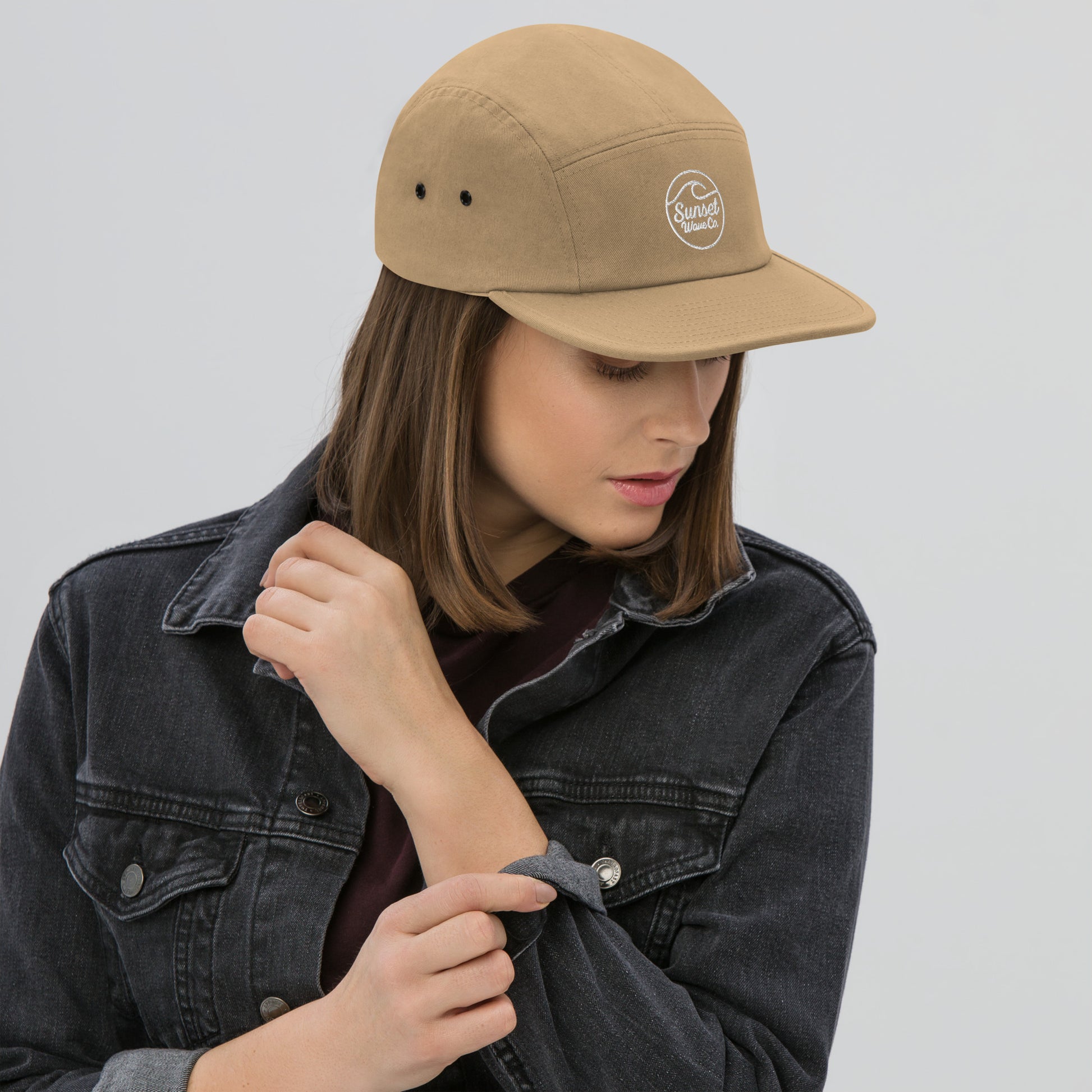 Woman wearing khaki 5-panel cap with white Sunset Wave Co. logo and black denim jacket