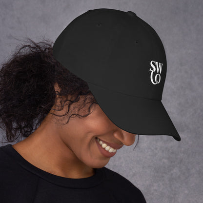 Smiling woman wearing a black dad hat with white SW and O logo on gray background