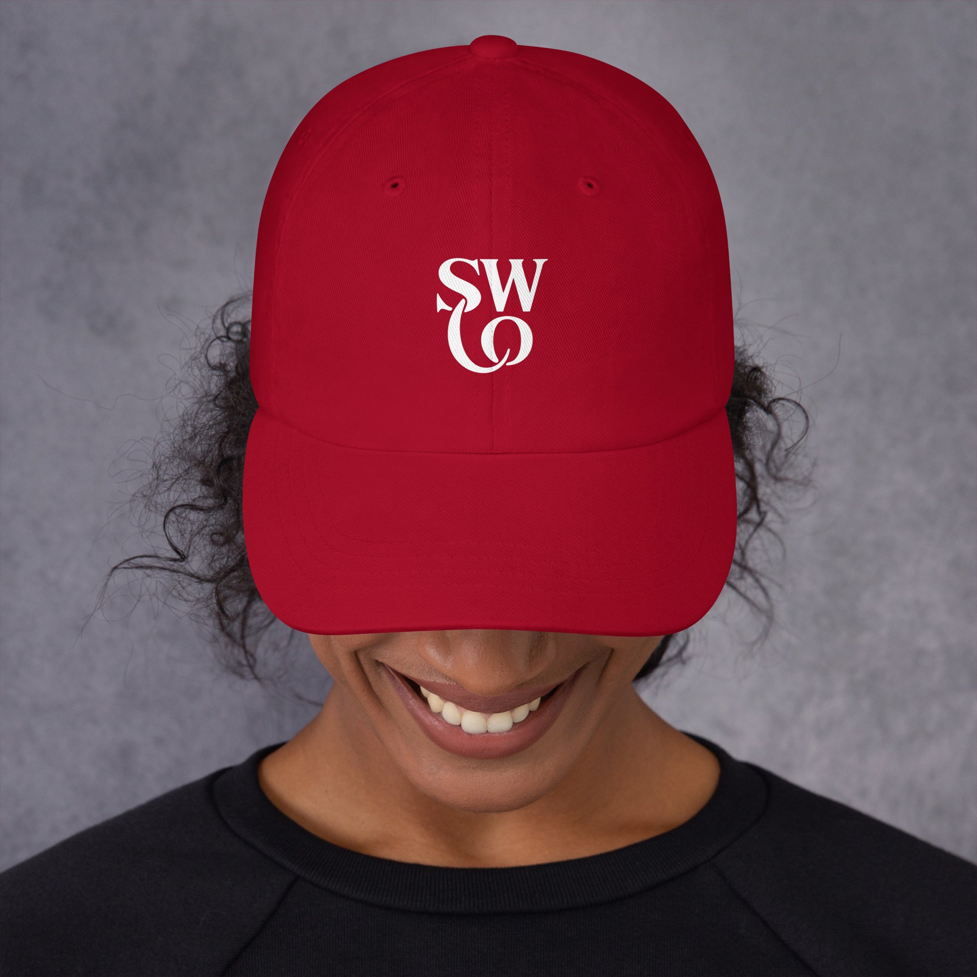 Smiling person wearing cranberry red dad hat with white SW logo on front and black shirt