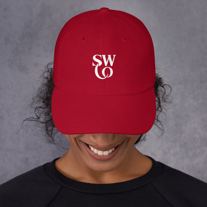 Smiling person wearing cranberry red dad hat with white SW logo on front and black shirt