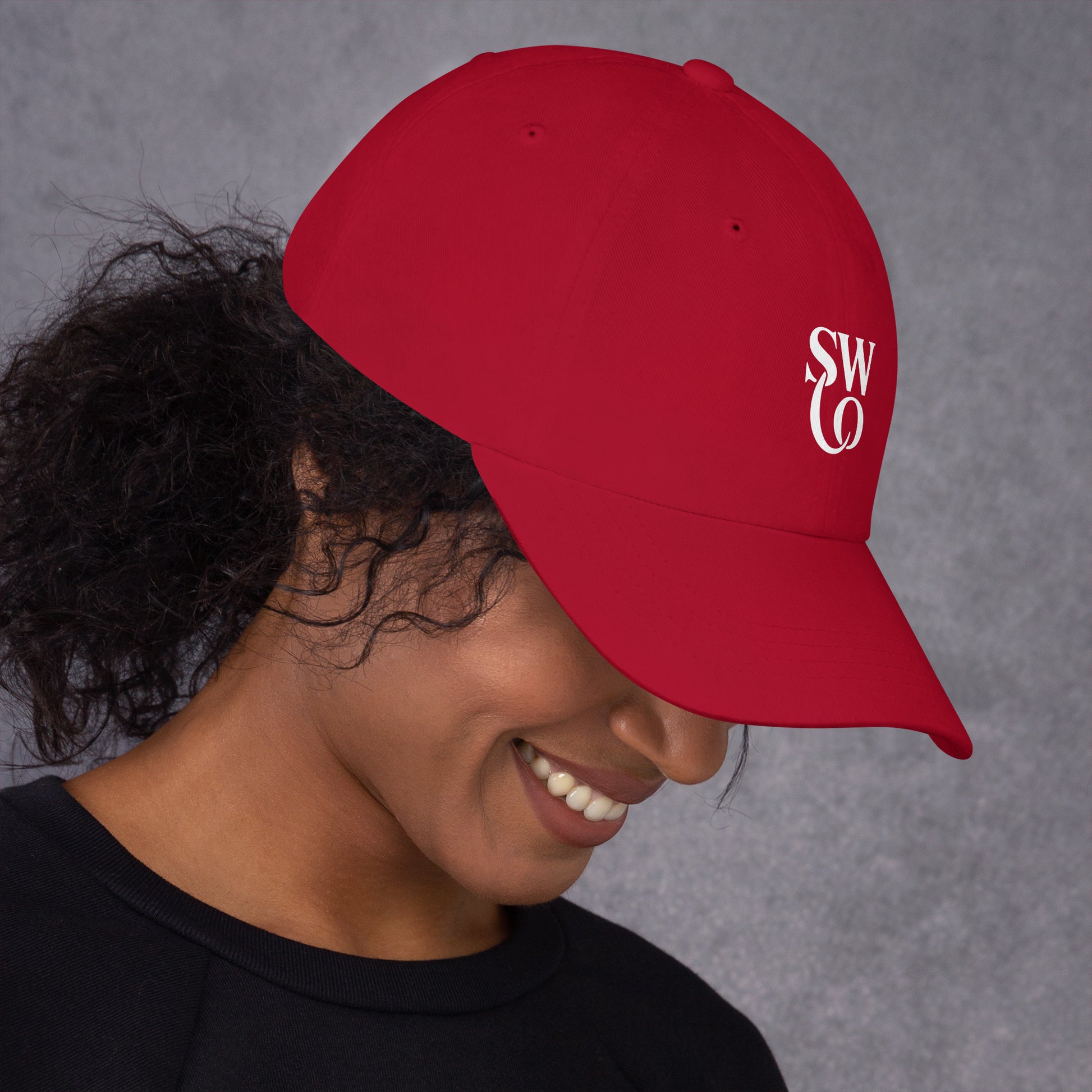 Smiling woman wearing cranberry red dad hat with white SWO logo on gray background