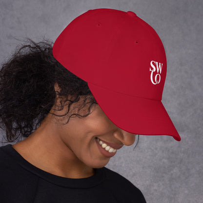 Smiling woman wearing cranberry red dad hat with white SWO logo on gray background