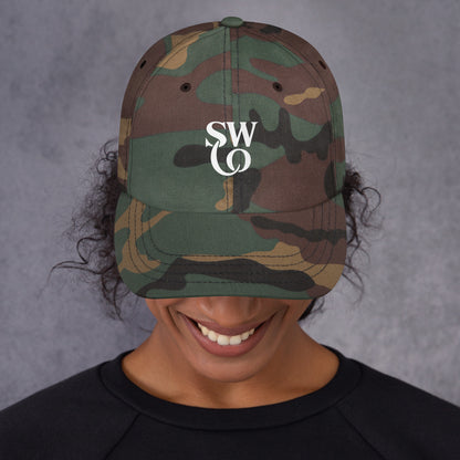 Smiling person wearing green camo classic dad hat with white SWO logo and black shirt