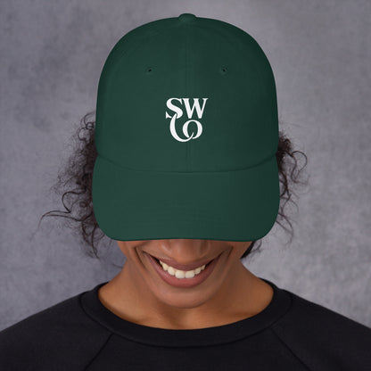 Smiling person wearing a spruce green dad hat with white stylish 'SWO' logo on front