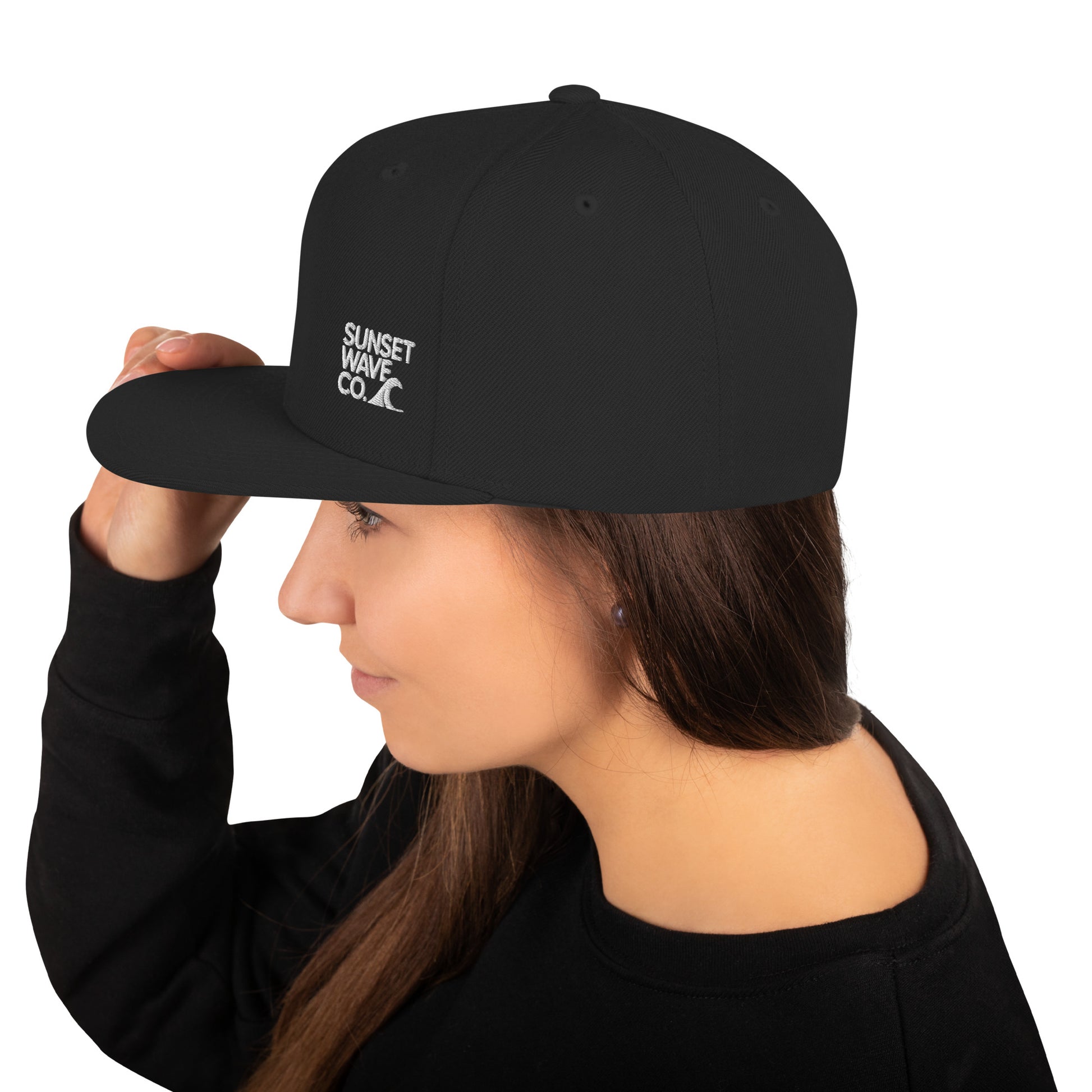 Black classic snapback cap with white Sunset Wave Co. logo worn by woman in black top
