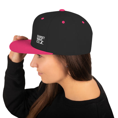 Woman wearing black and neon pink snapback hat with Sunset Wave Co. logo on side