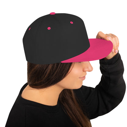 Woman wearing black snapback hat with neon pink visor and button, holding hat brim