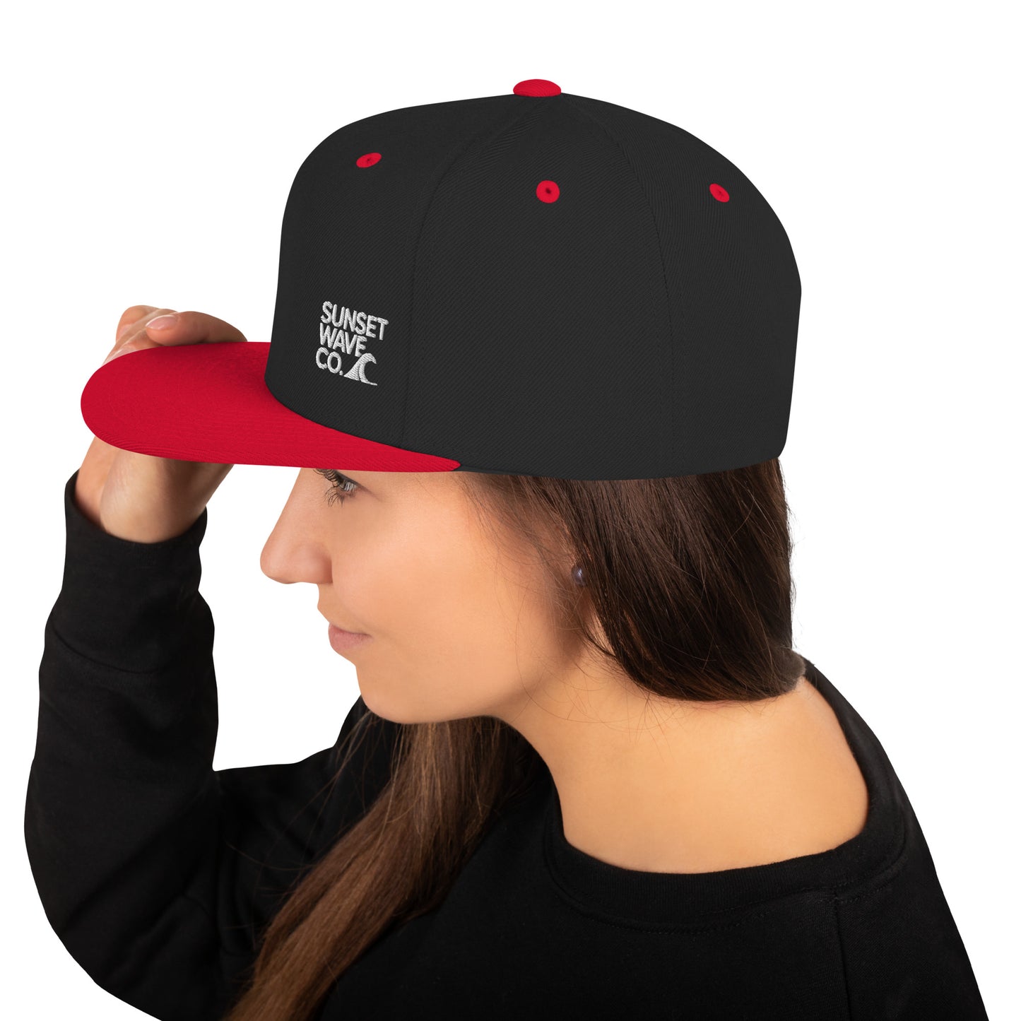 Black and red snapback cap with Sunset Wave Co. logo worn by woman in black sweatshirt