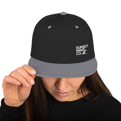 Woman wearing black and gray snapback hat with white Sunset Wave Co. logo
