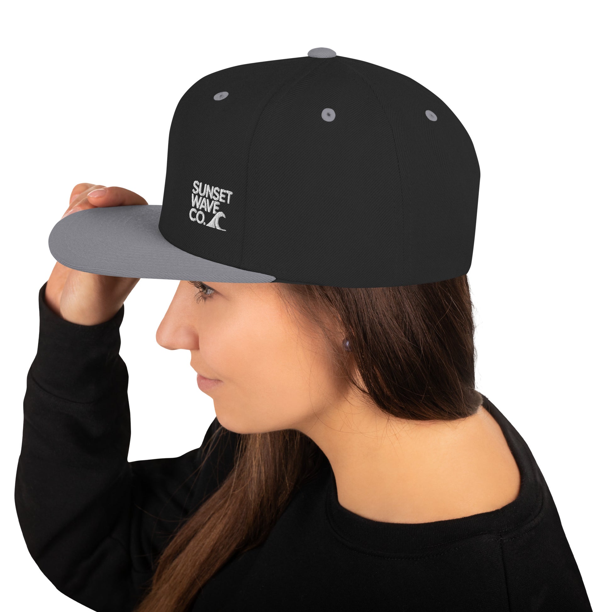 Woman wearing black and gray classic snapback cap with Sunset Wave Co. logo, side view