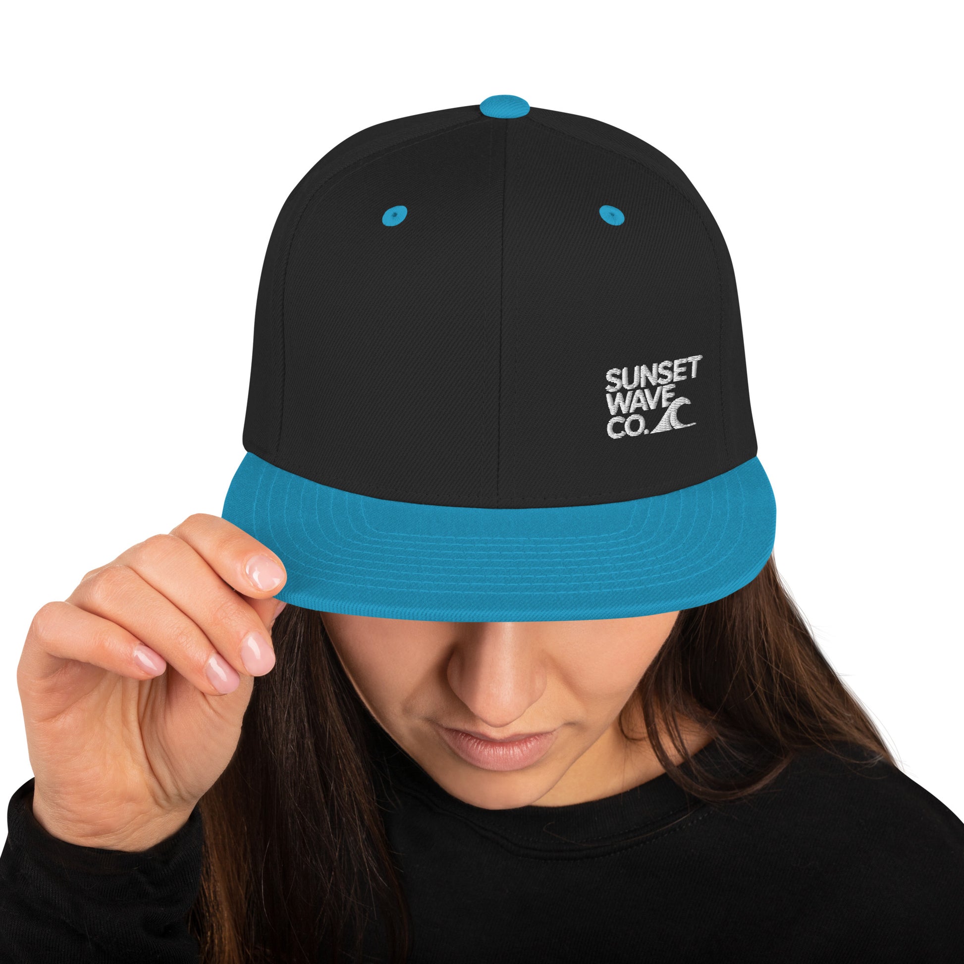 Black and teal classic snapback hat with Sunset Wave Co. logo worn by woman adjusting brim
