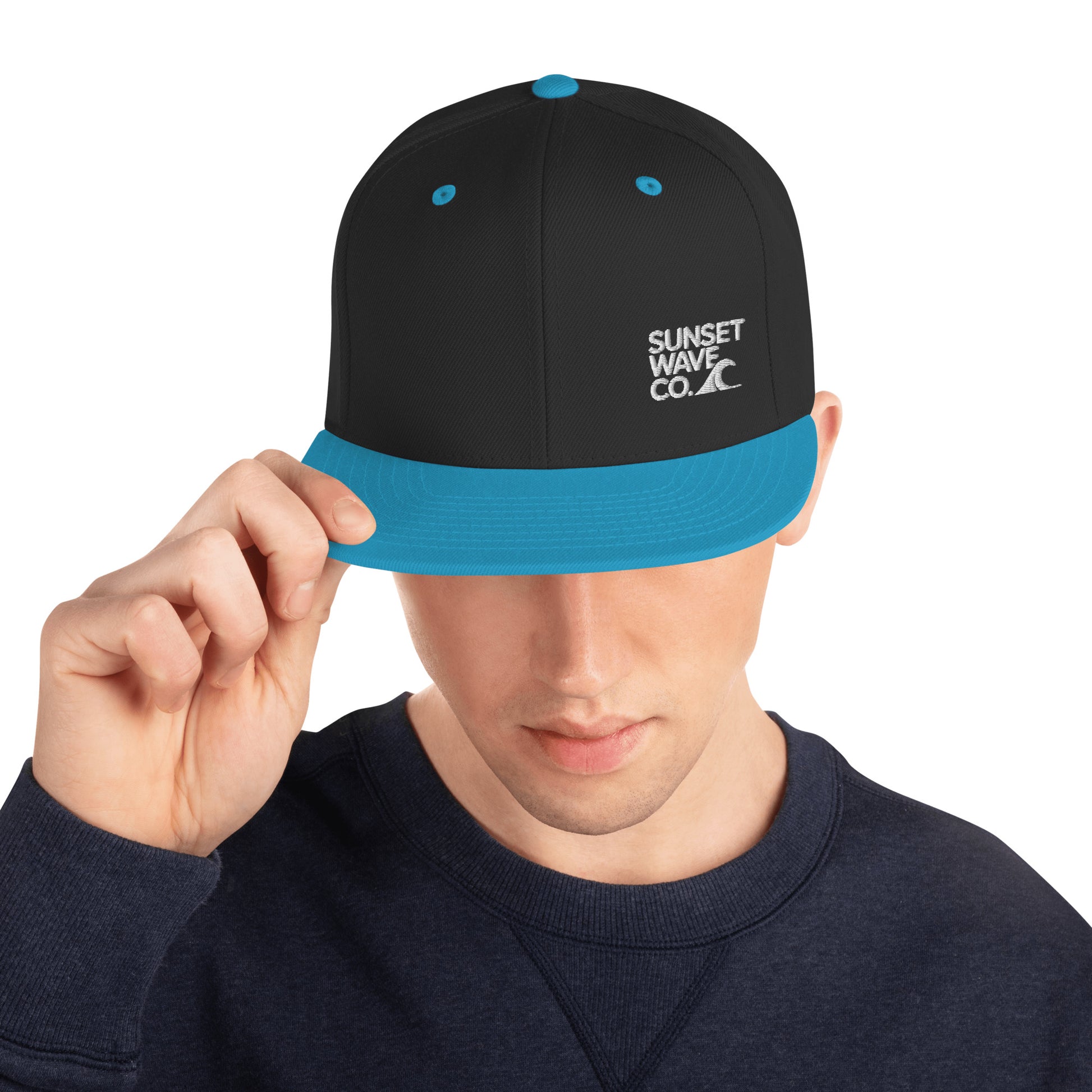Man wearing black and teal snapback hat with Sunset Wave Co. logo, navy sweatshirt