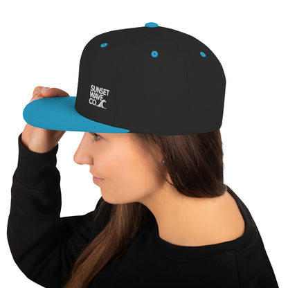 Woman wearing black and teal snapback cap with Sunset Wave Co. logo on the side