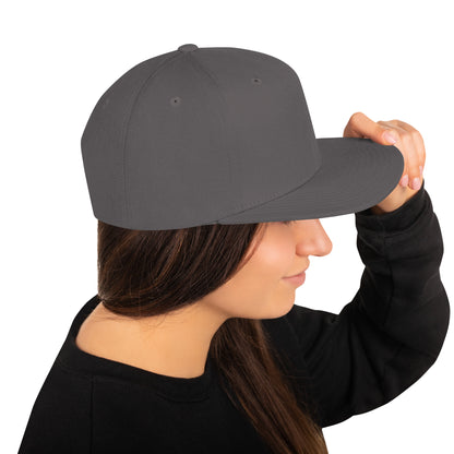 Woman wearing dark grey classic snapback hat holding brim in profile on white background