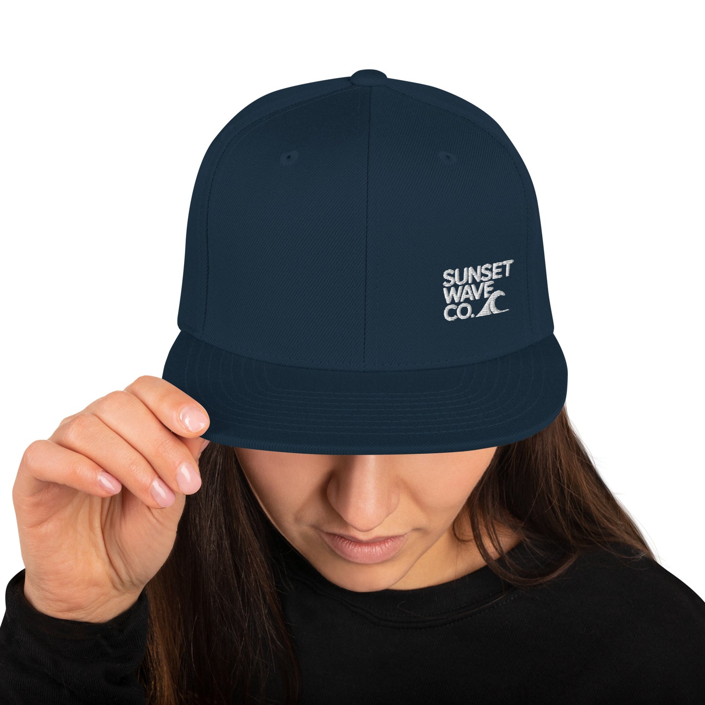 Dark navy classic snapback hat with white Sunset Wave Co. logo worn by woman adjusting brim