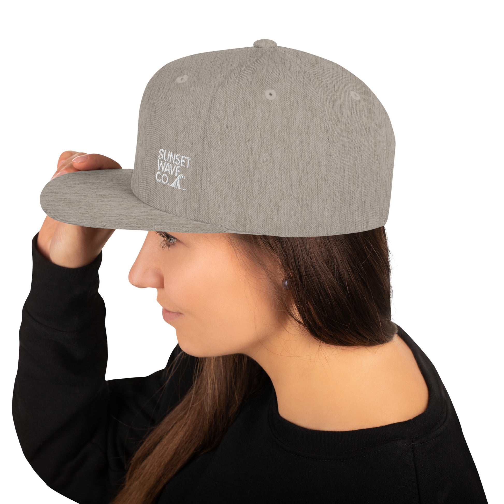 Heather grey classic snapback cap with Sunset Wave Co. logo worn by woman in black sweatshirt
