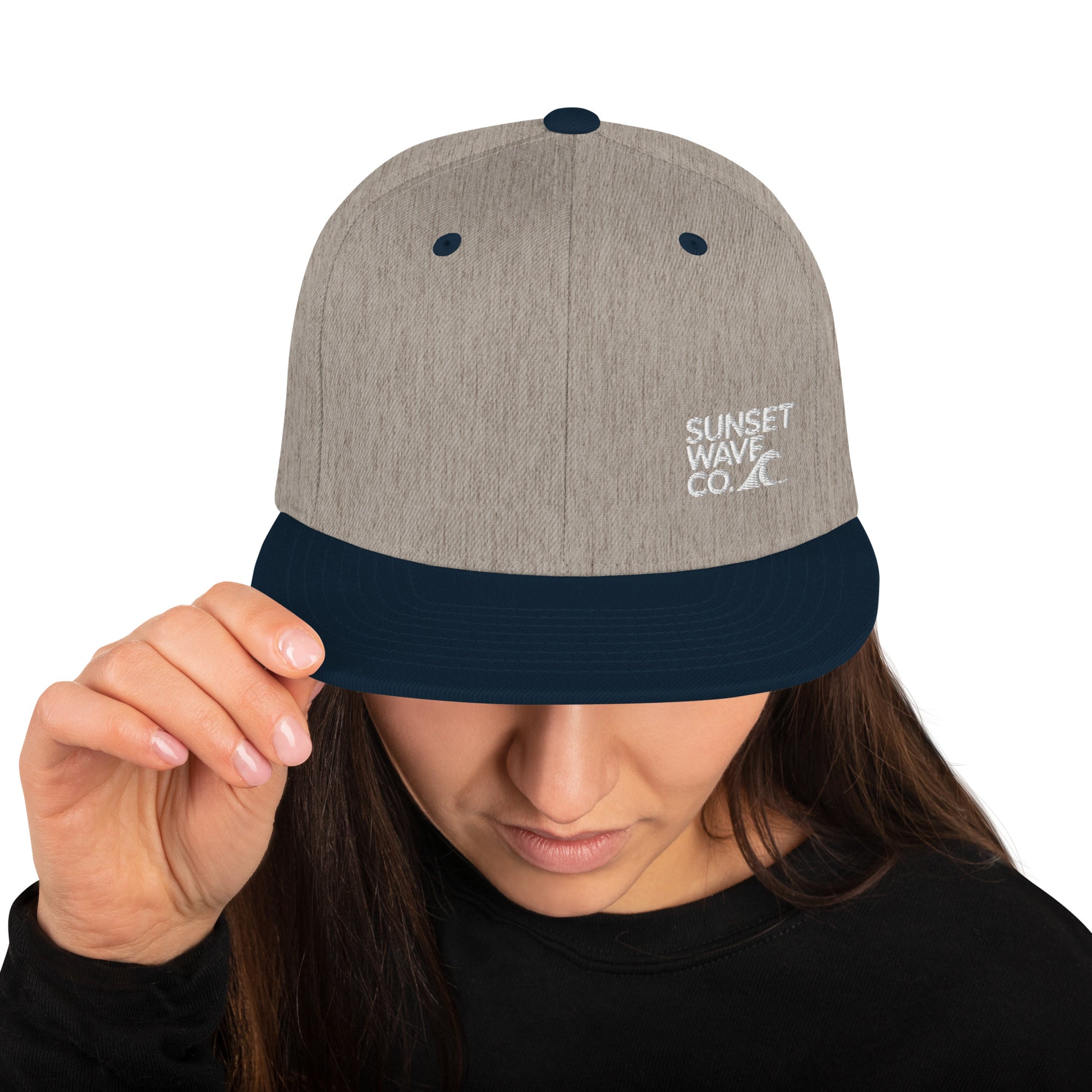 Heather grey and navy snapback hat with Sunset Wave Co. logo worn by woman holding brim