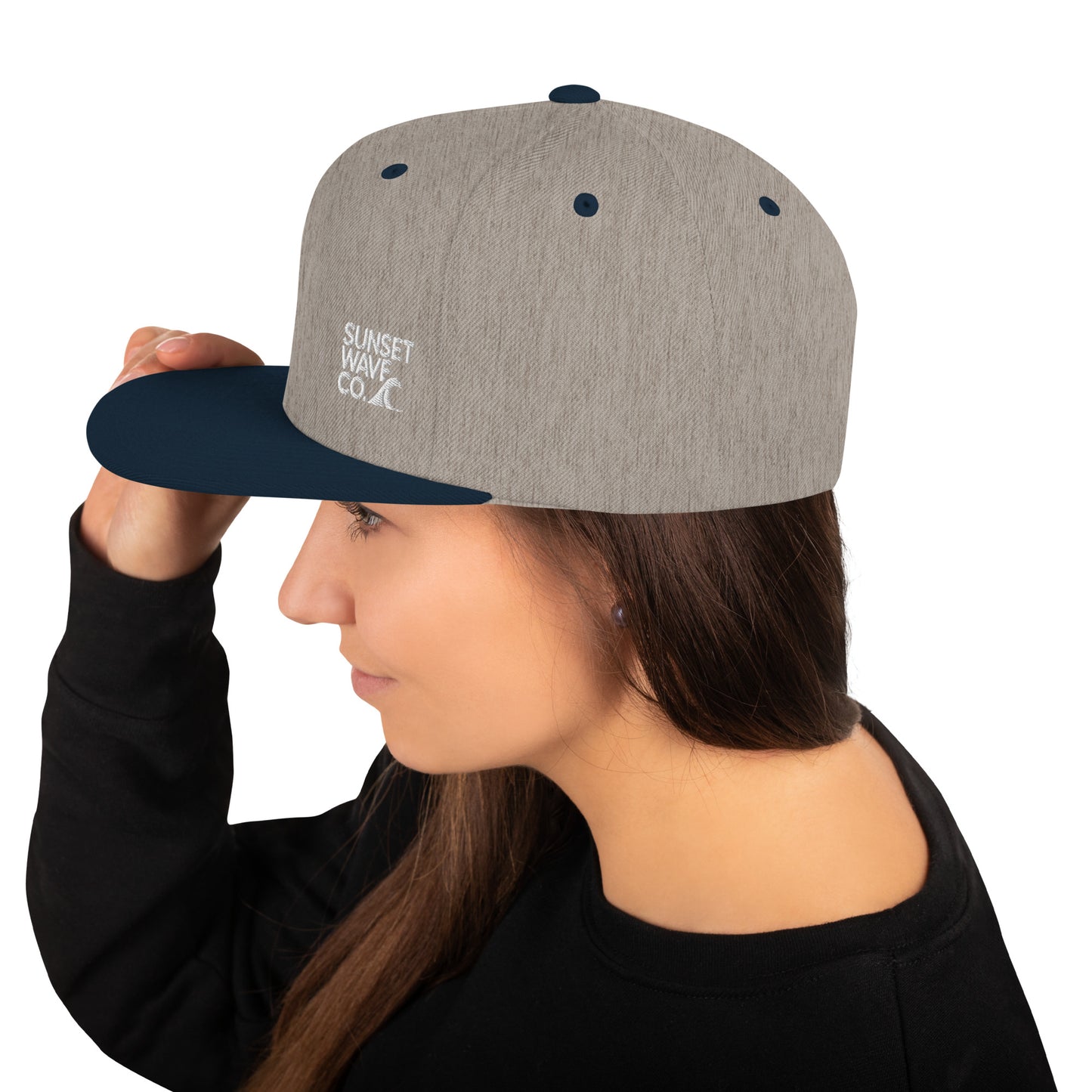 Woman wearing grey and navy snapback cap with Sunset Wave Co. logo, side profile on white background