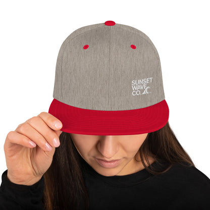 Heather grey and red classic snapback cap with Sunset Wave Co. logo worn by woman in black top