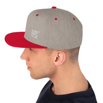 Side view of man wearing heather grey snapback cap with red brim and embroidered Sunset Wave Co. logo