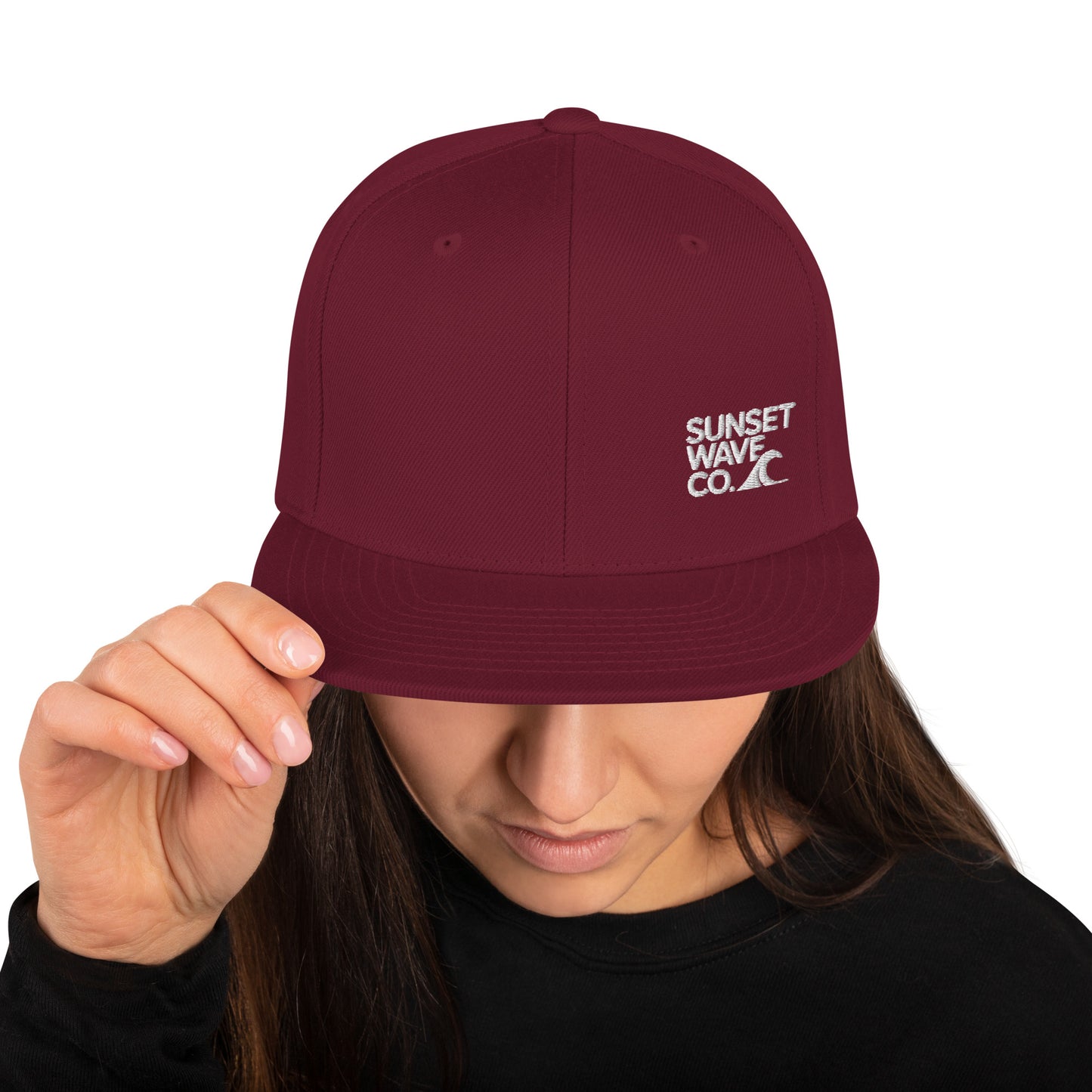 Maroon classic snapback hat with white embroidered Sunset Wave Co. logo worn by woman in black shirt
