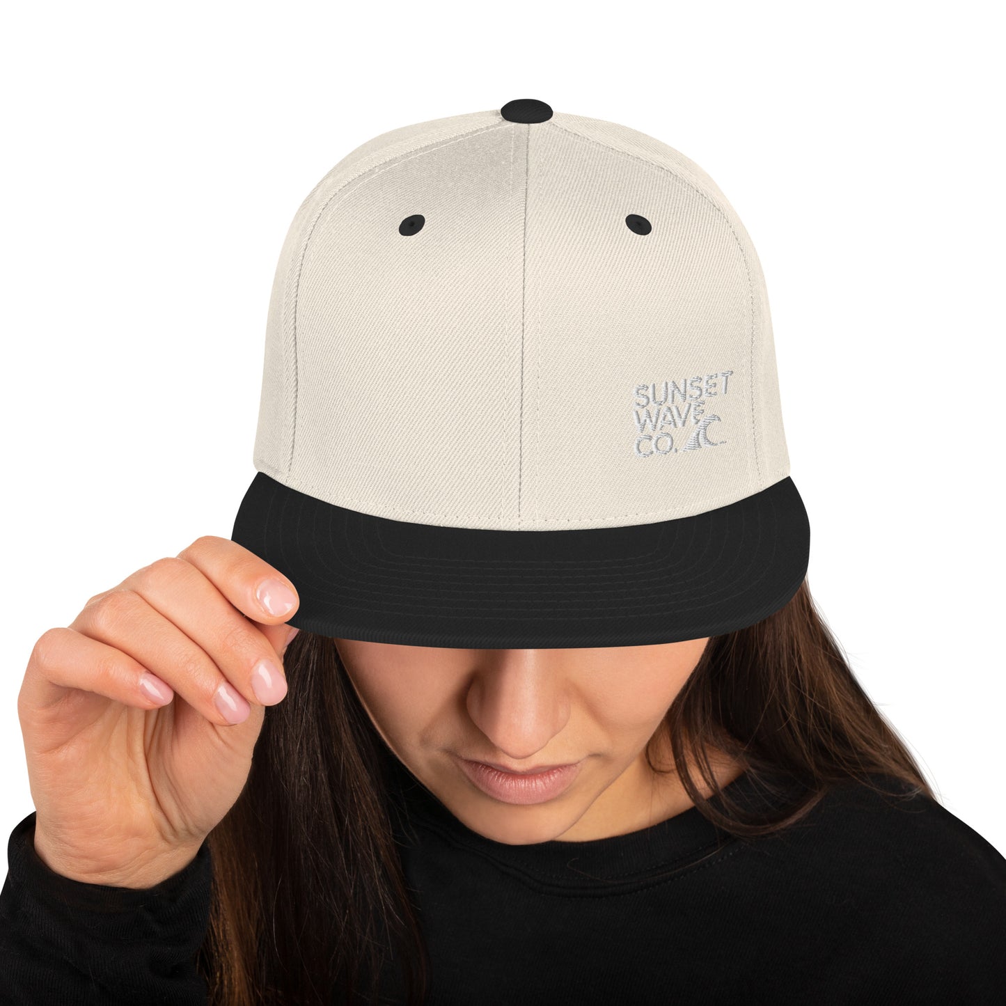Woman wearing a natural color snapback hat with black brim and embroidered Sunset Wave Co. logo