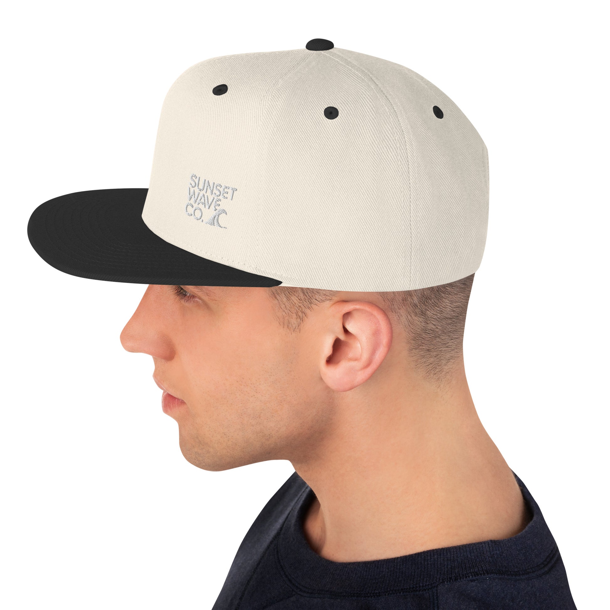 Side view of man wearing beige and black classic snapback hat with Sunset Wave Co. logo