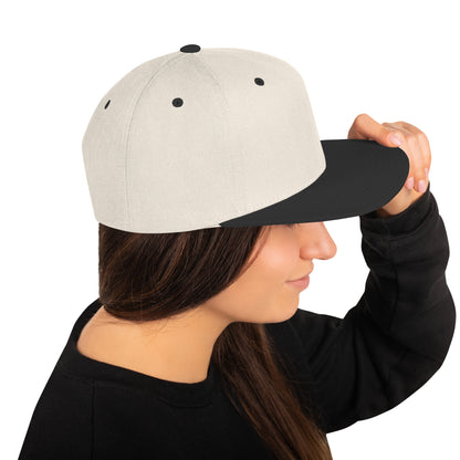 Woman wearing a natural color snapback cap with black brim and black eyelets, holding the brim
