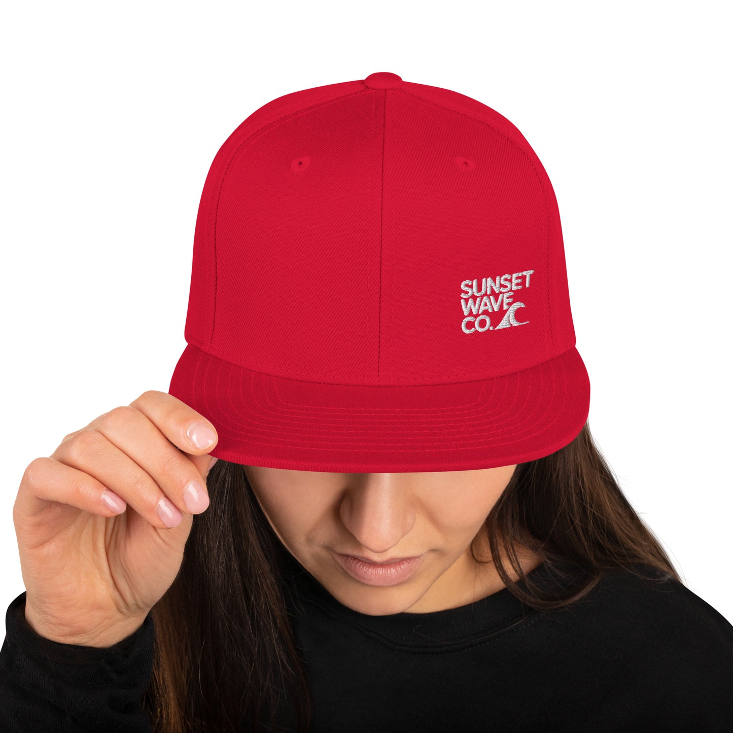Person wearing red snapback hat with white Sunset Wave Co. logo, holding brim, black shirt