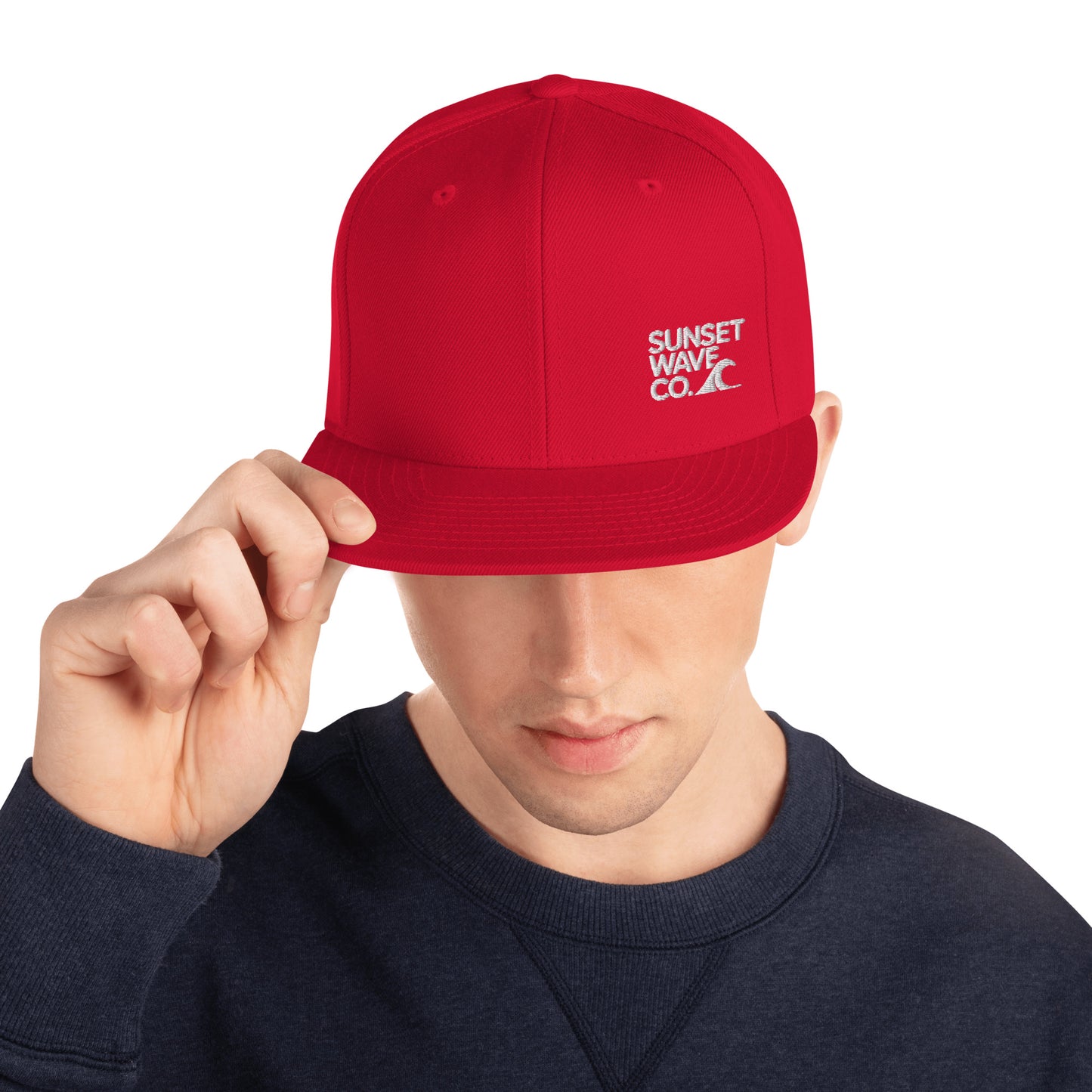 Man wearing red classic snapback hat with white Sunset Wave Co. logo, navy sweatshirt