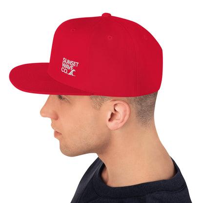 Side view of man wearing red snapback hat with white Sunset Wave Co. logo and wave graphic