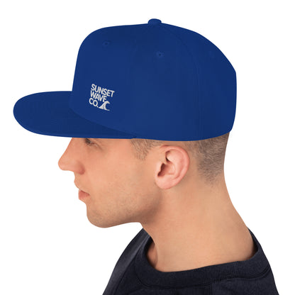 Side view of a man wearing a royal blue classic snapback hat with white Sunset Wave Co. logo