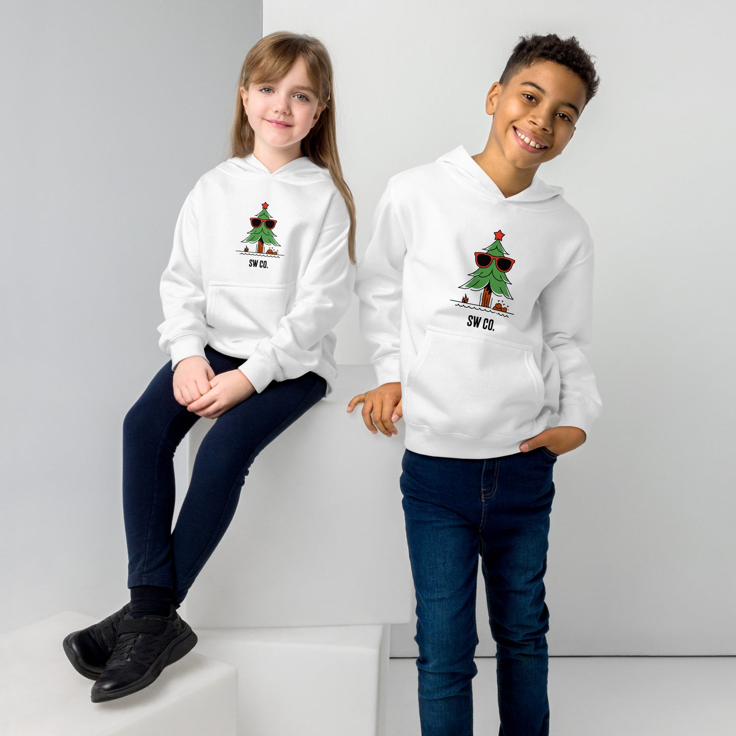 Two children wearing white fleece hoodies with sunglasses Christmas tree design, posing in studio