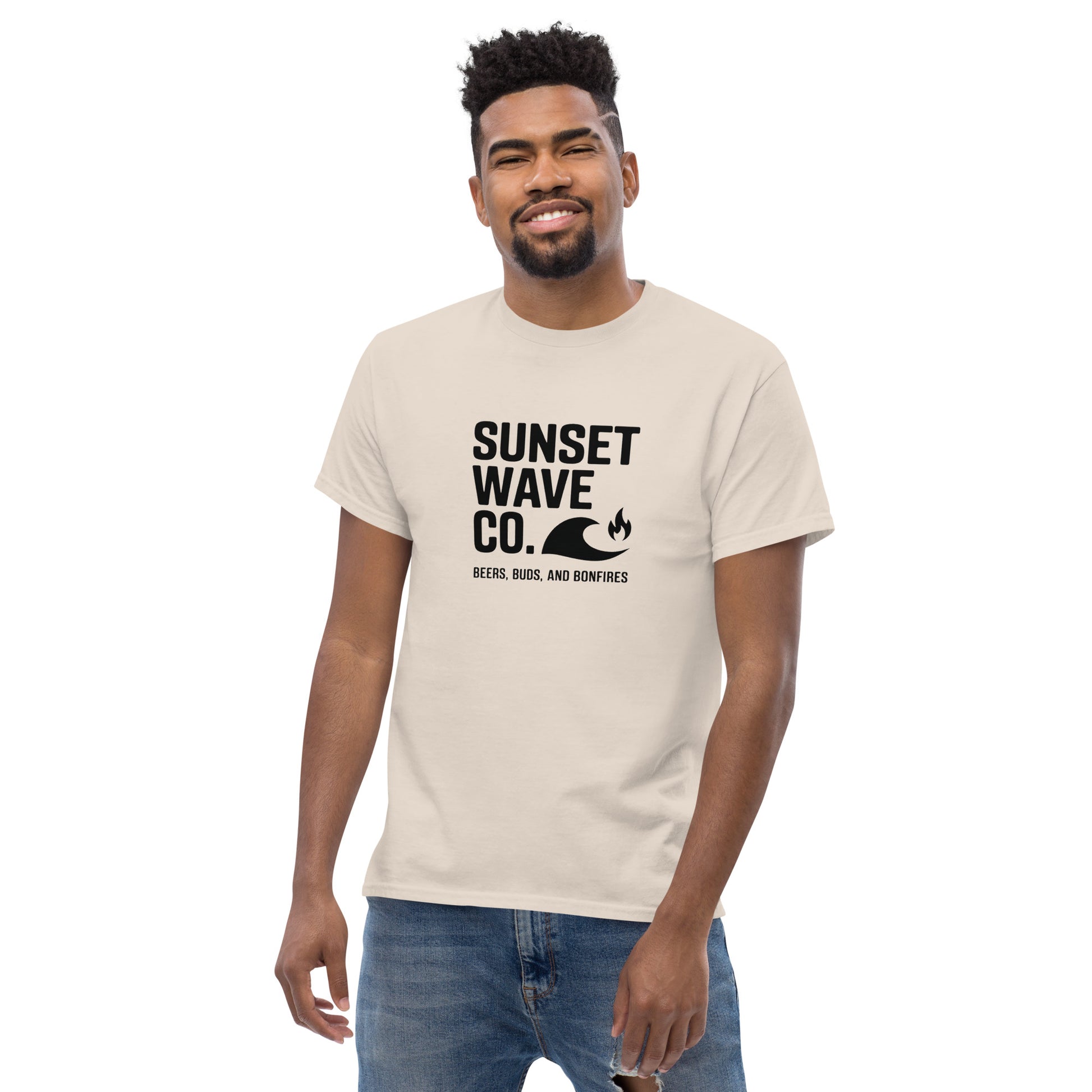 Smiling man wearing a natural color unisex tee with black Sunset Wave Co. logo and jeans