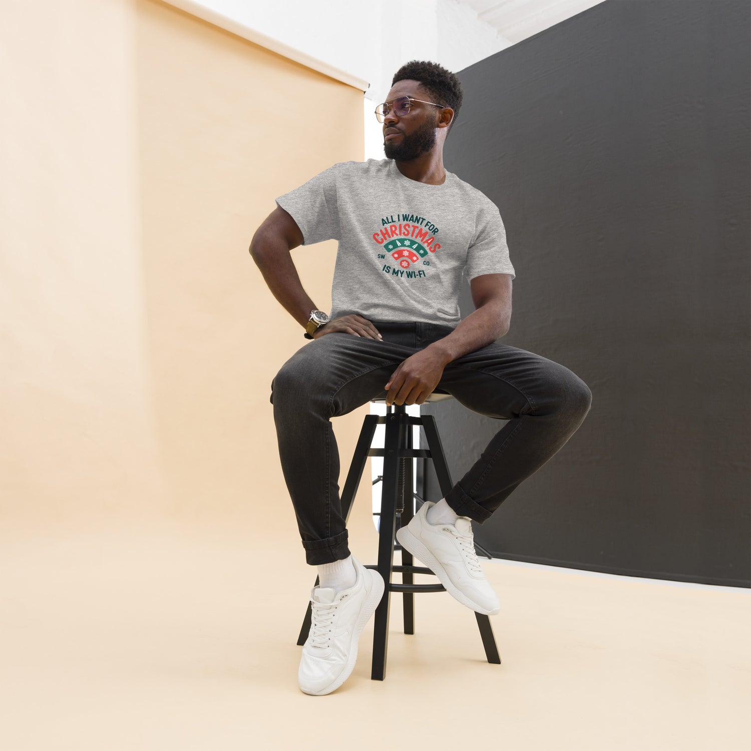 Man wearing sport grey unisex Christmas Wi-Fi graphic tee, seated on stool in studio
