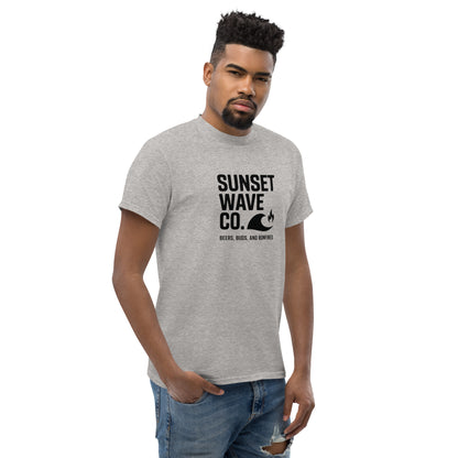 Man wearing sport grey classic unisex t-shirt with Sunset Wave Co. graphic and jeans with torn knee