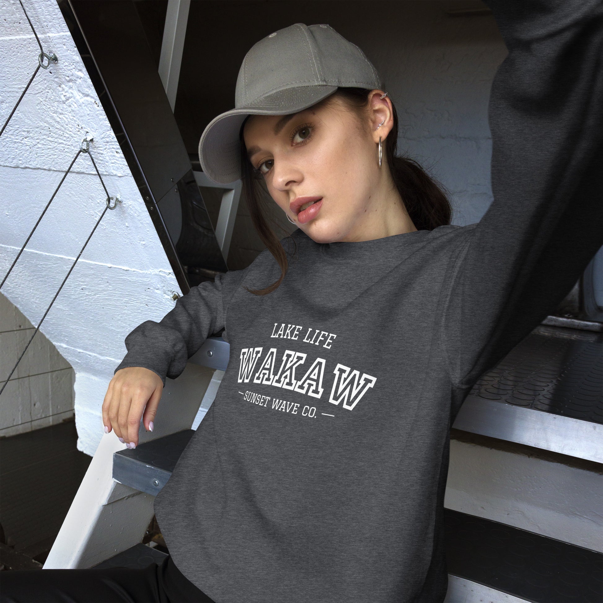 Woman wearing dark heather unisex crew neck sweatshirt with WAKA W lake life print and gray cap