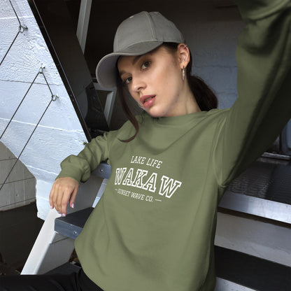 Young woman in military green crew neck sweatshirt with WAKAW text, posing on indoor metal stairs