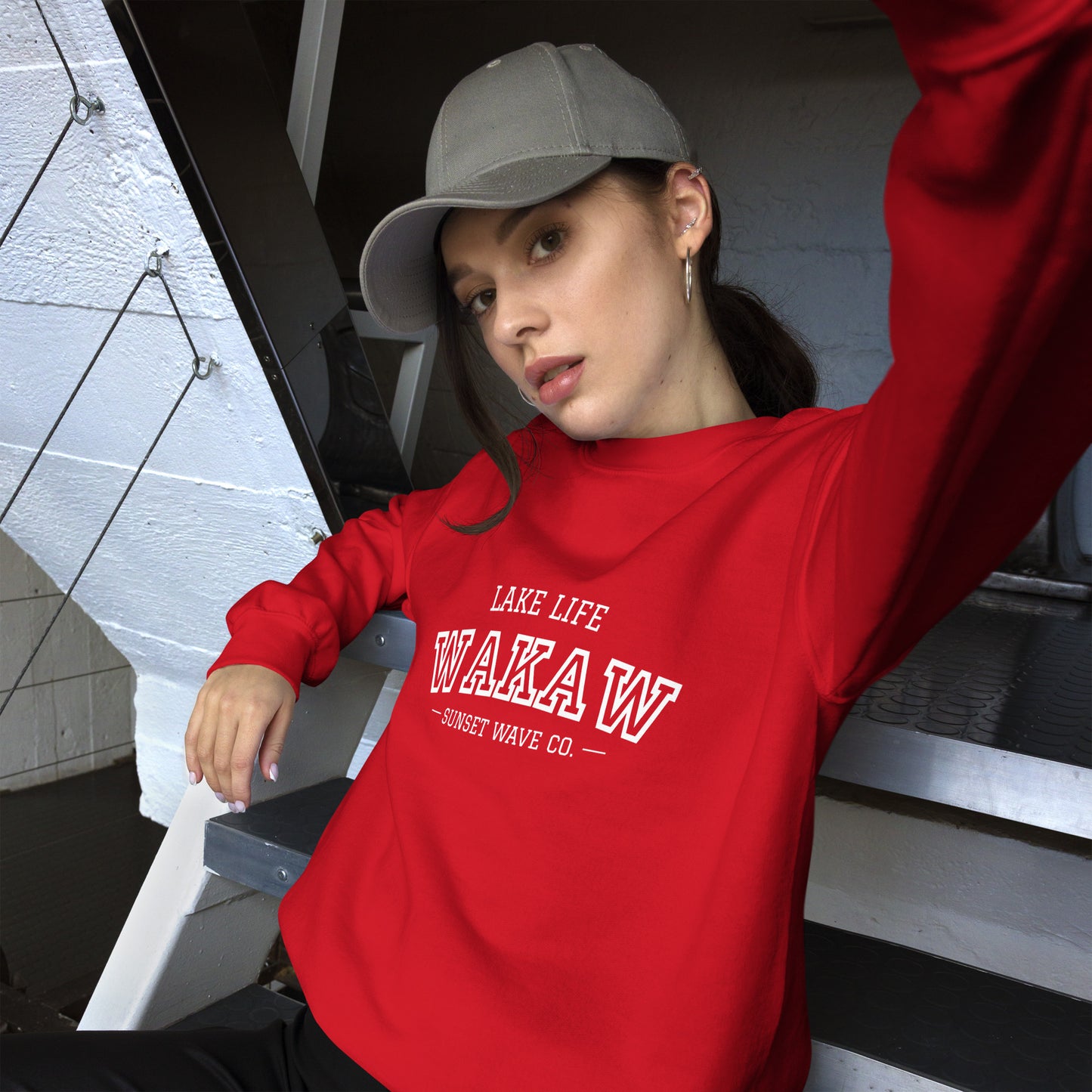 Young woman wearing a red unisex crew neck sweatshirt with white text and a gray baseball cap