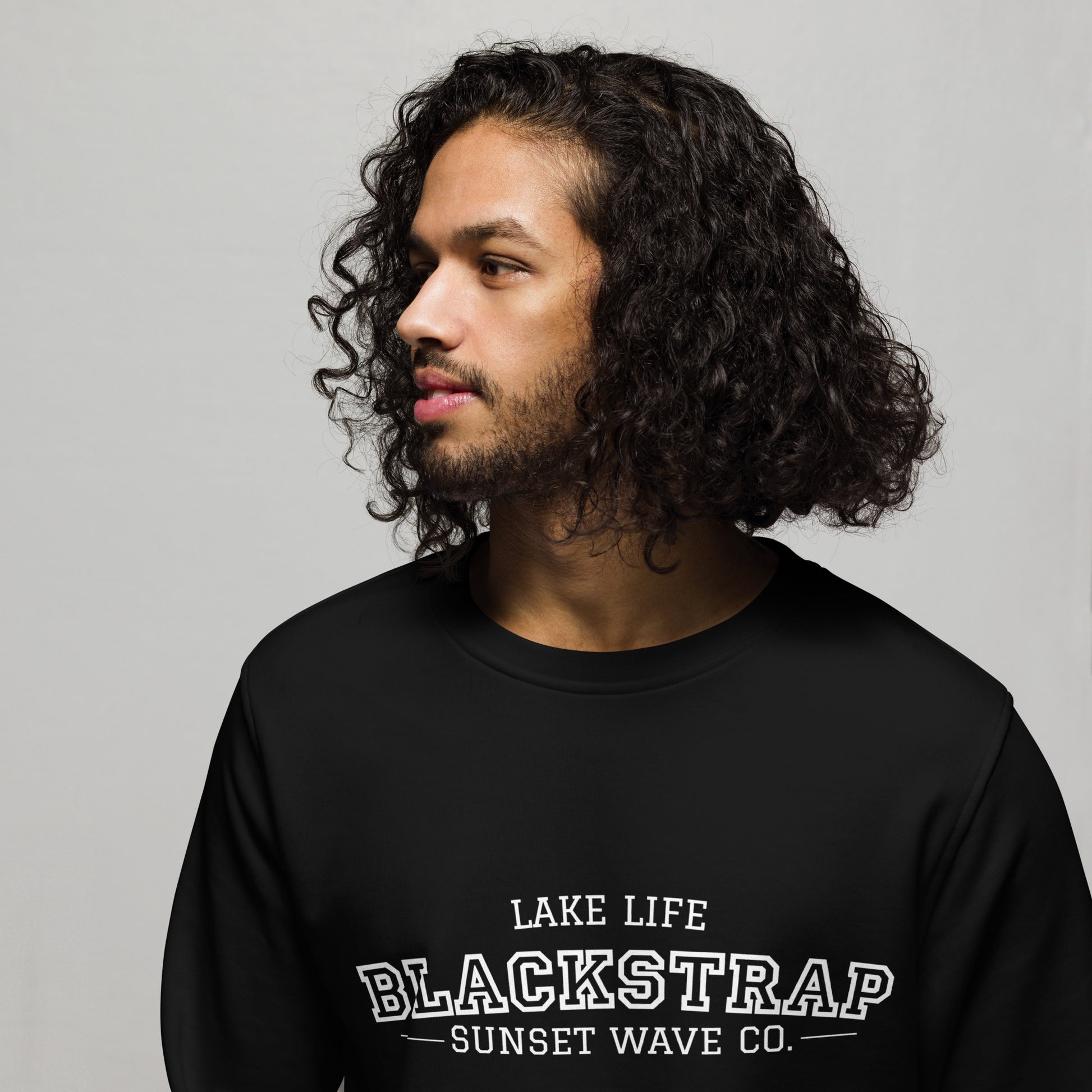 Man wearing black organic sweatshirt with white text 'Lake Life Blackstrap Sunset Wave Co.' on front