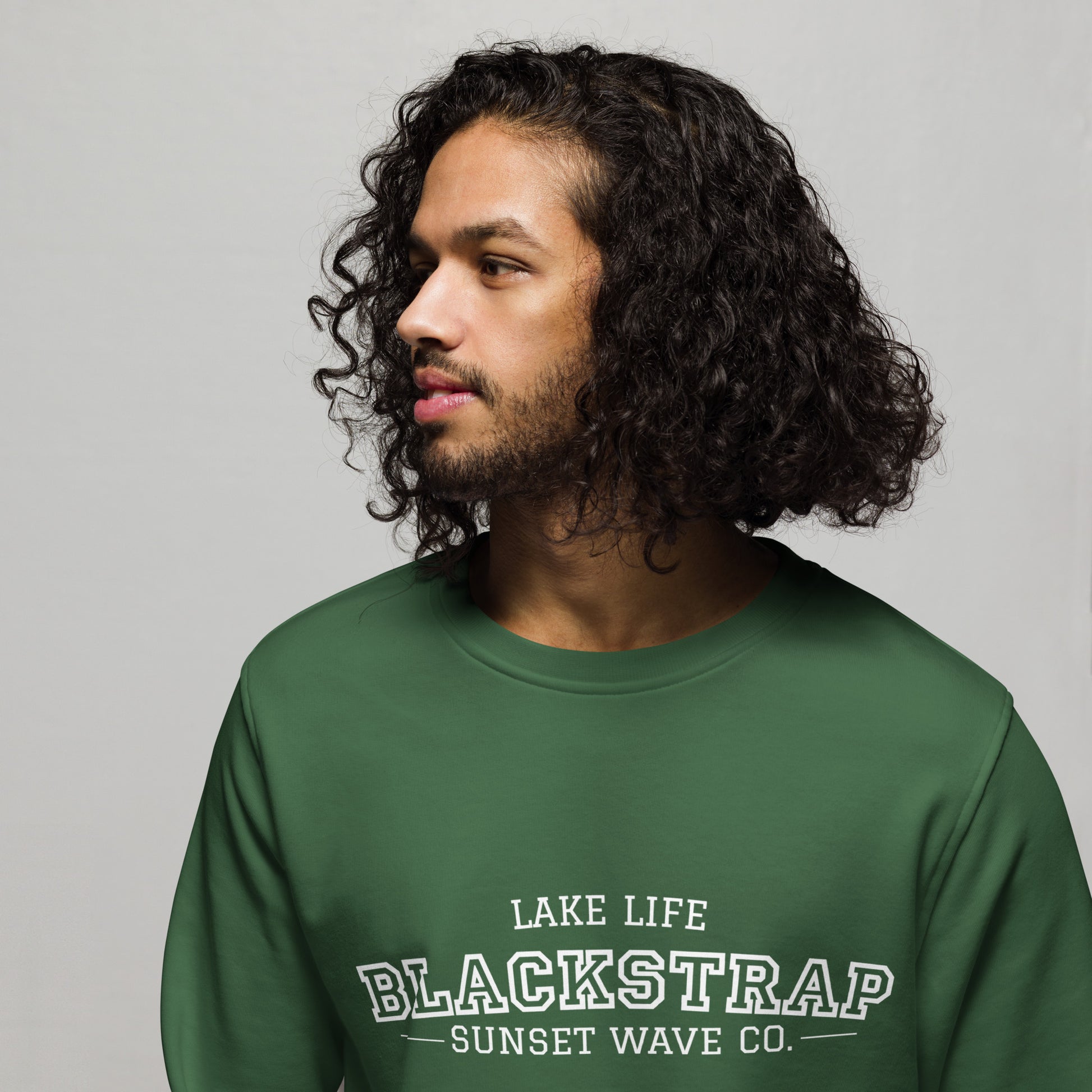 Man with curly hair wearing a bottle green unisex organic sweatshirt with Blackstrap logo
