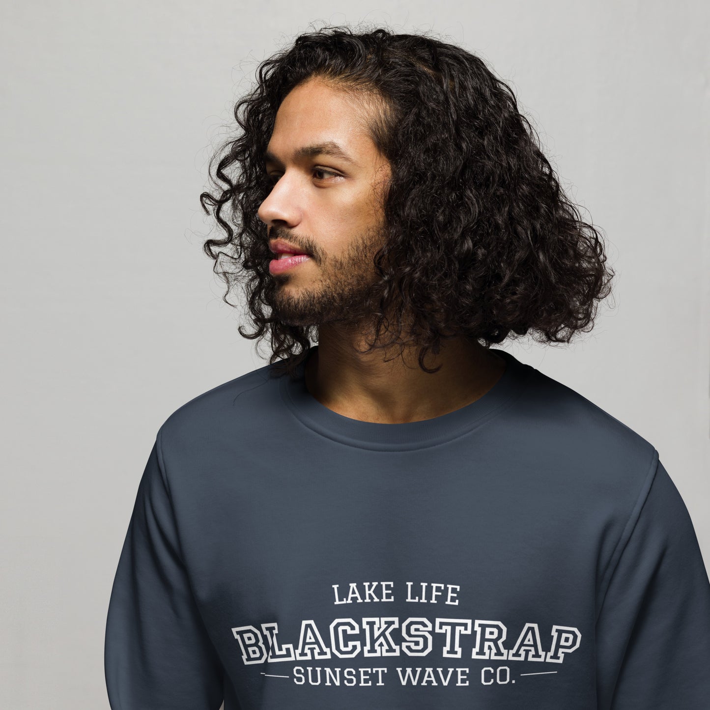 Man with curly hair wearing a french navy sweatshirt with Blackstrap Lake Life Sunset Wave Co. logo