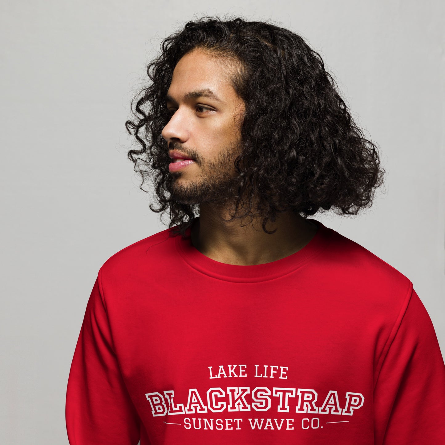 Man with curly hair wearing red organic sweatshirt with 'Blackstrap Lake Life Sunset Wave Co.' text