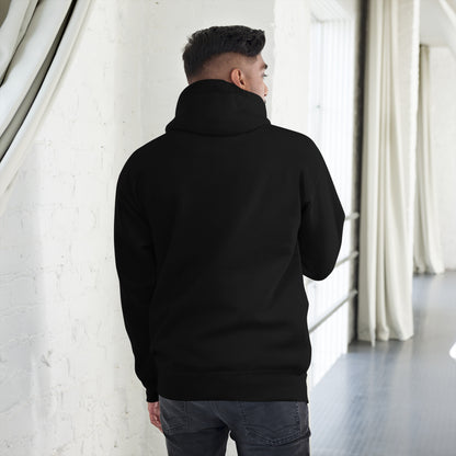 Man wearing black unisex premium hoodie standing indoors with white brick wall backdrop
