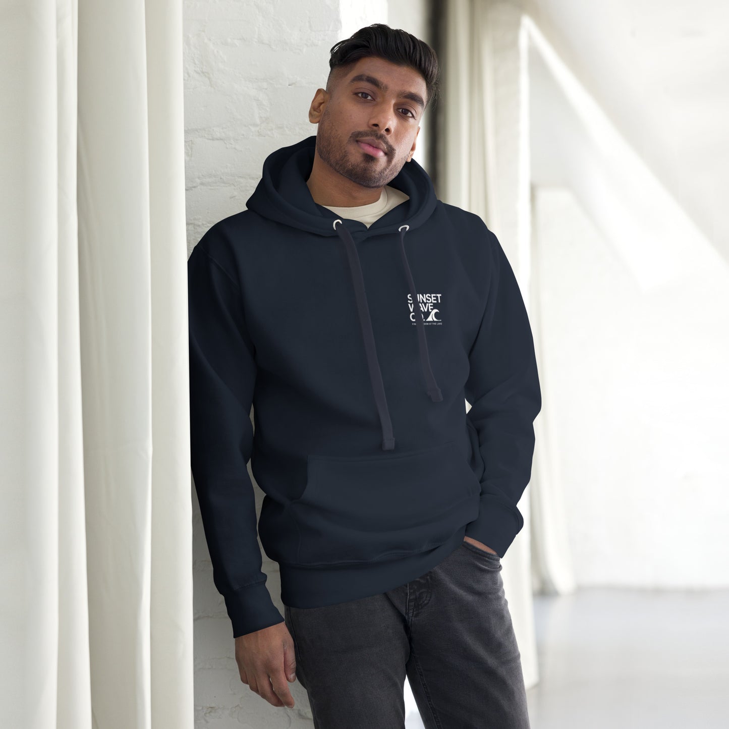 Man wearing navy blue unisex premium hoodie with front pocket and white text logo standing indoors