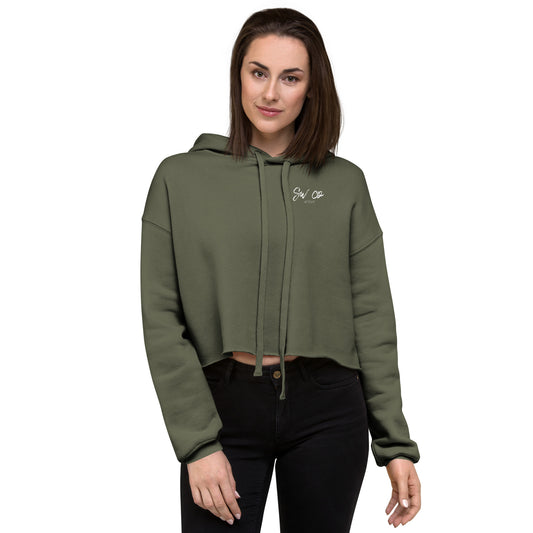 Woman wearing military green cropped hoodie with drawstrings and small white logo, paired with black pants